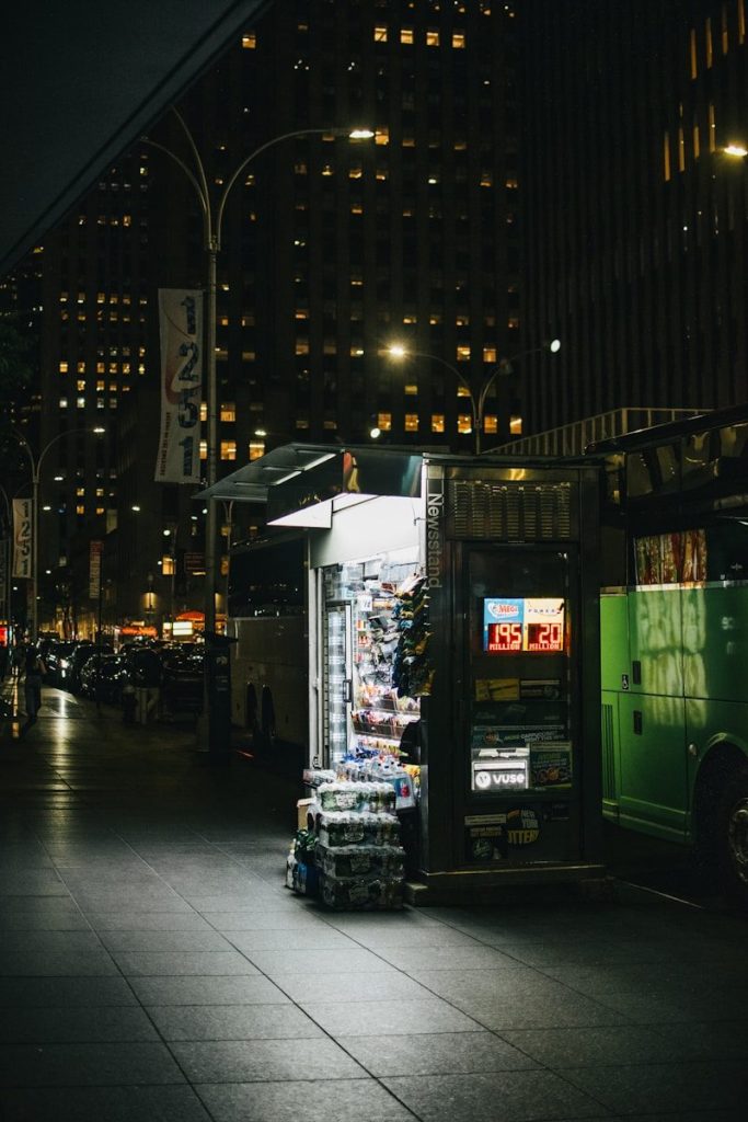 Brightly lit newsstand on a city street at night.