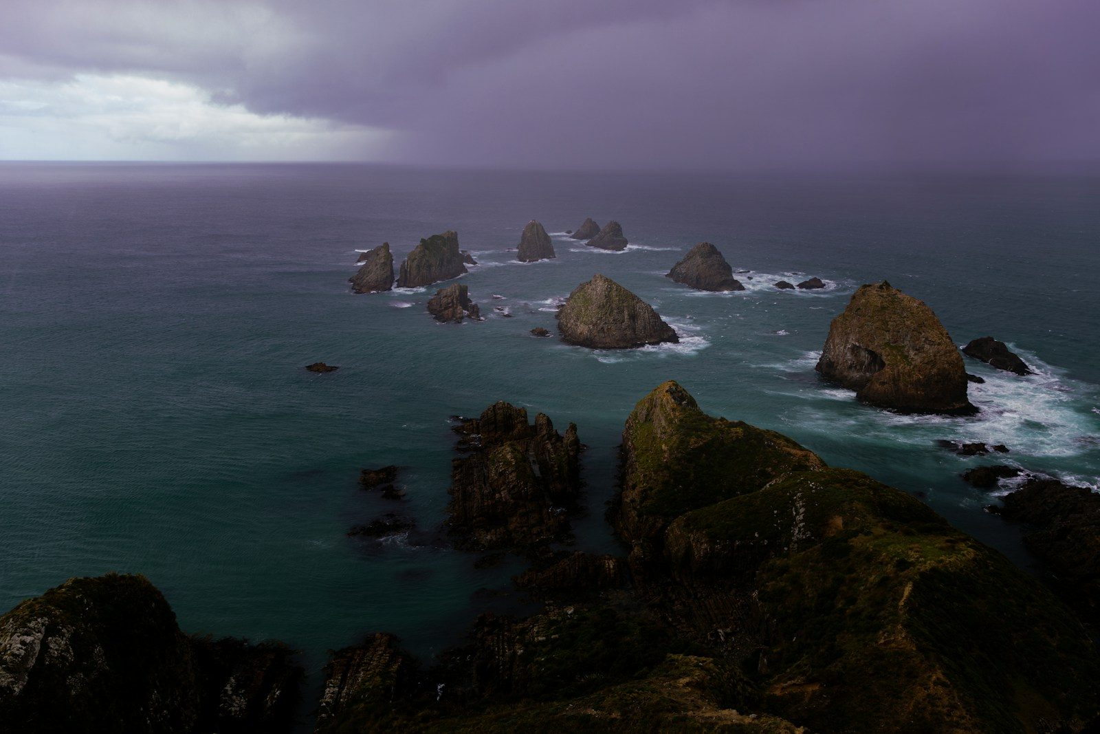 Jagged rock formations rise from the ocean under stormy skies.