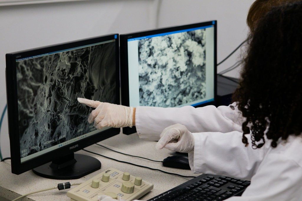Scientist points to microscopic view on computer screen.