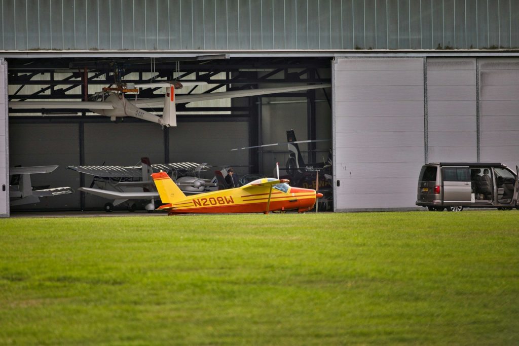 Small airplane parked in an open hangar with a van.