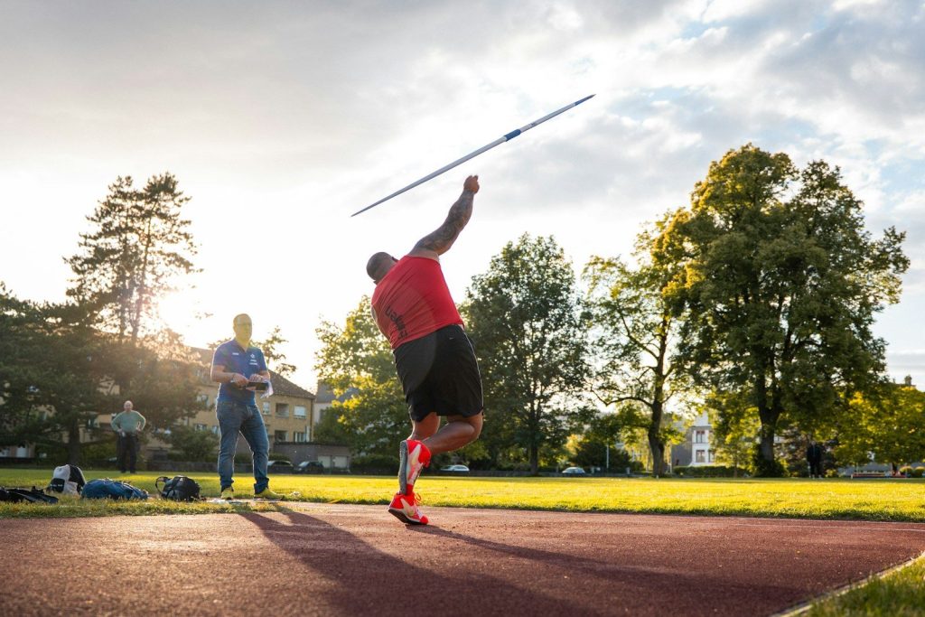 Athlete throwing a javelin on a track at sunset.
