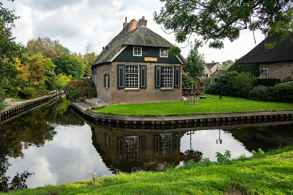 Thatched roof house by a canal with reflection