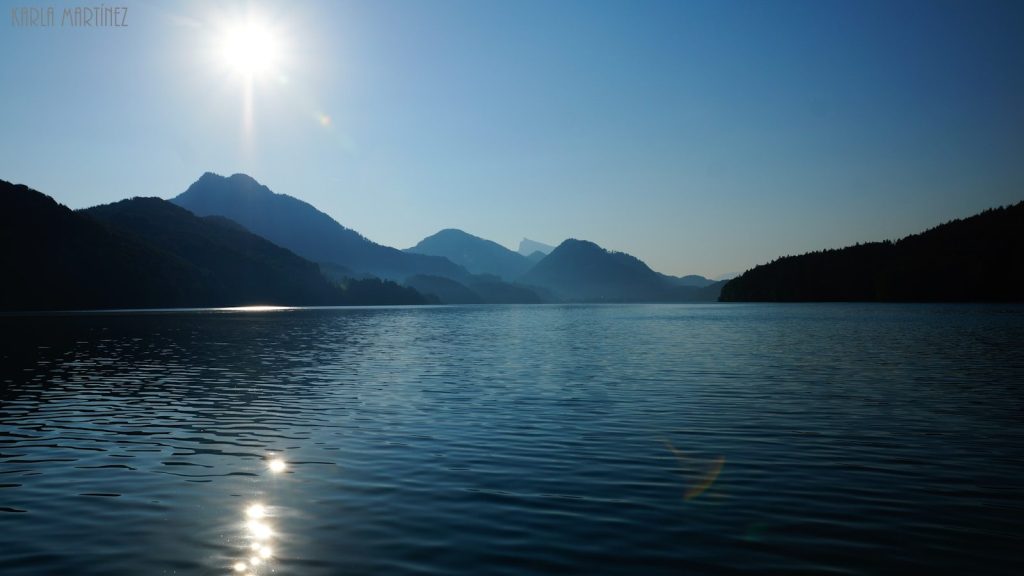 Sunlight reflects on a calm lake with mountains.