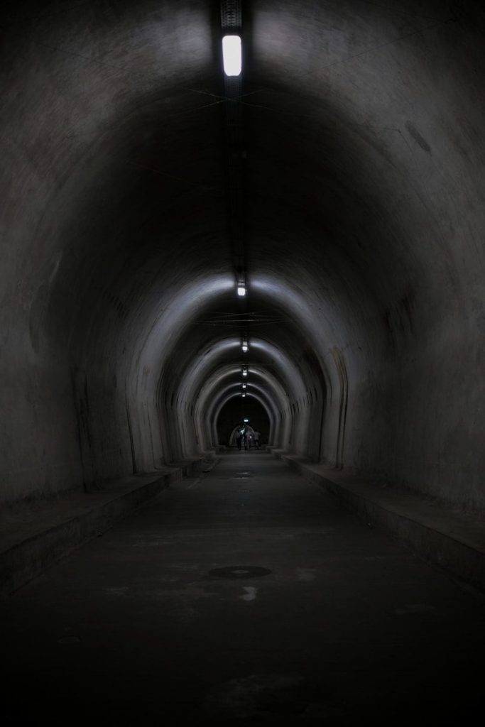 A long, dark tunnel with arched ceilings and overhead lights.