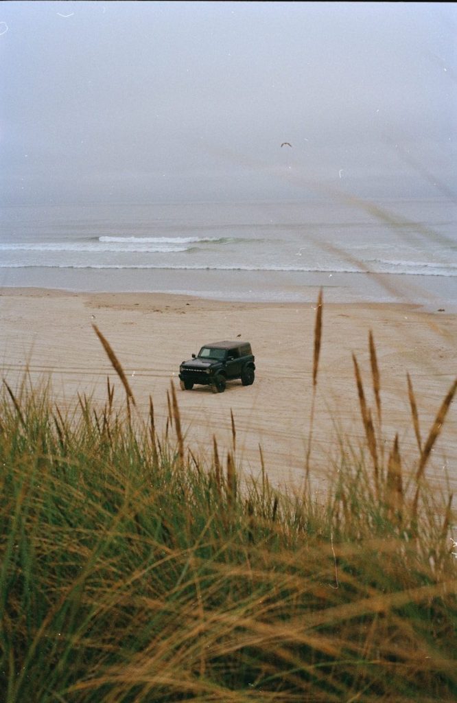 Dark suv parked on a sandy beach near ocean waves.