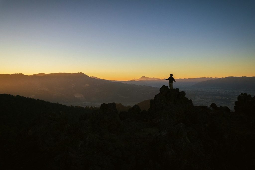 A person stands on a mountain peak at sunrise.