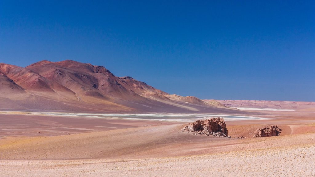 brown sand field near brown mountain under blue sky during daytime