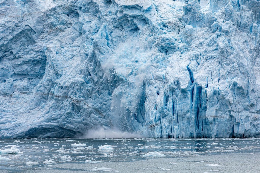 Massive glacier calving into icy water, creating a large splash.