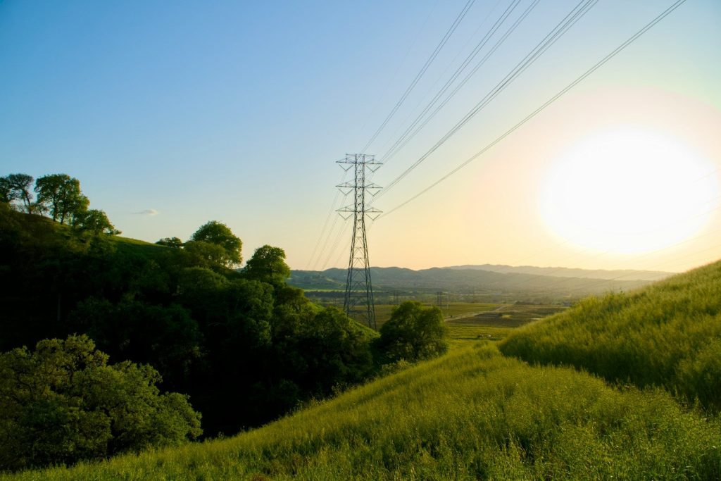 Power lines cross a grassy hill at sunset.