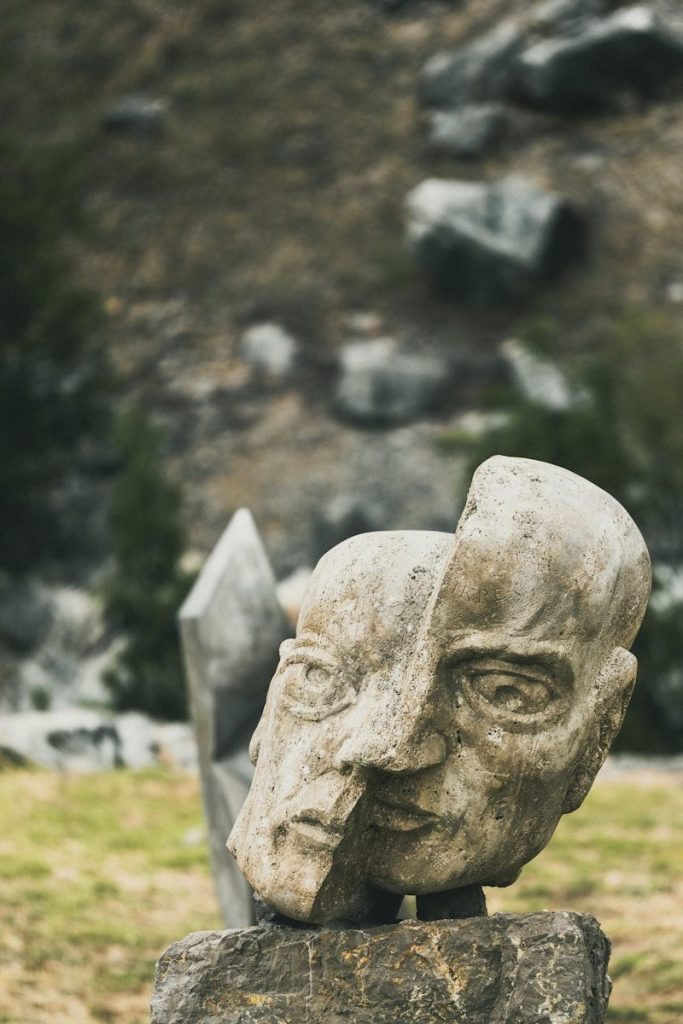 A stone sculpture of a split human head outdoors.