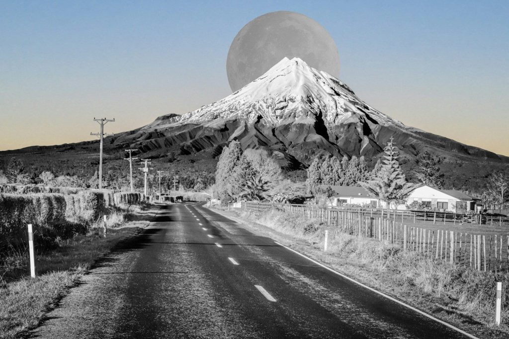 Road leads to snow-capped mountain under large moon.