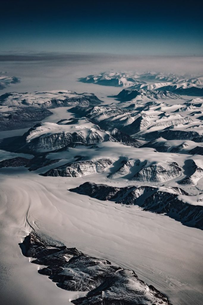 Dramatic aerial shot of a vast snow-covered mountain range under a clear sky, captured in winter.