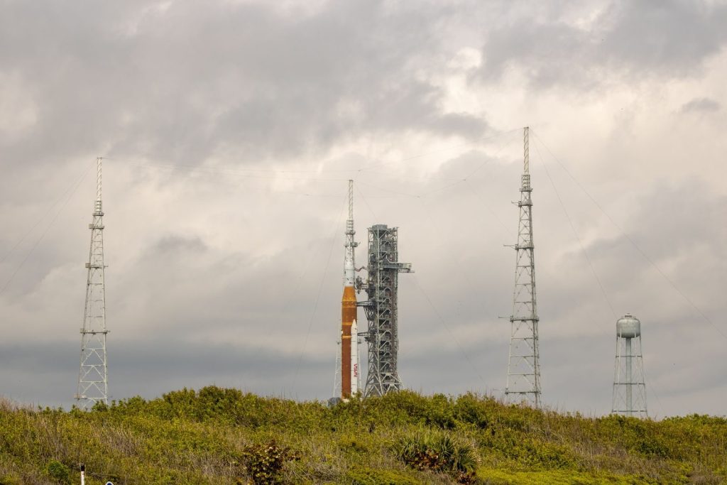 NASA rocket on launch pad surrounded by antennas against a cloudy sky.