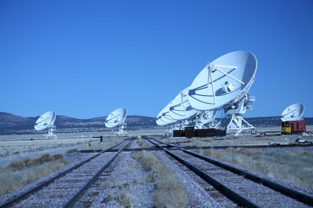 Array of satellite dishes in rural landscape with clear blue sky, showcasing advanced technology.