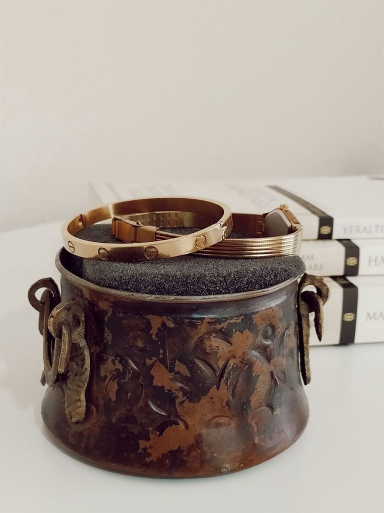 Close-up of elegant gold bracelets resting on a weathered antique vase, perfect for jewelry enthusiasts.