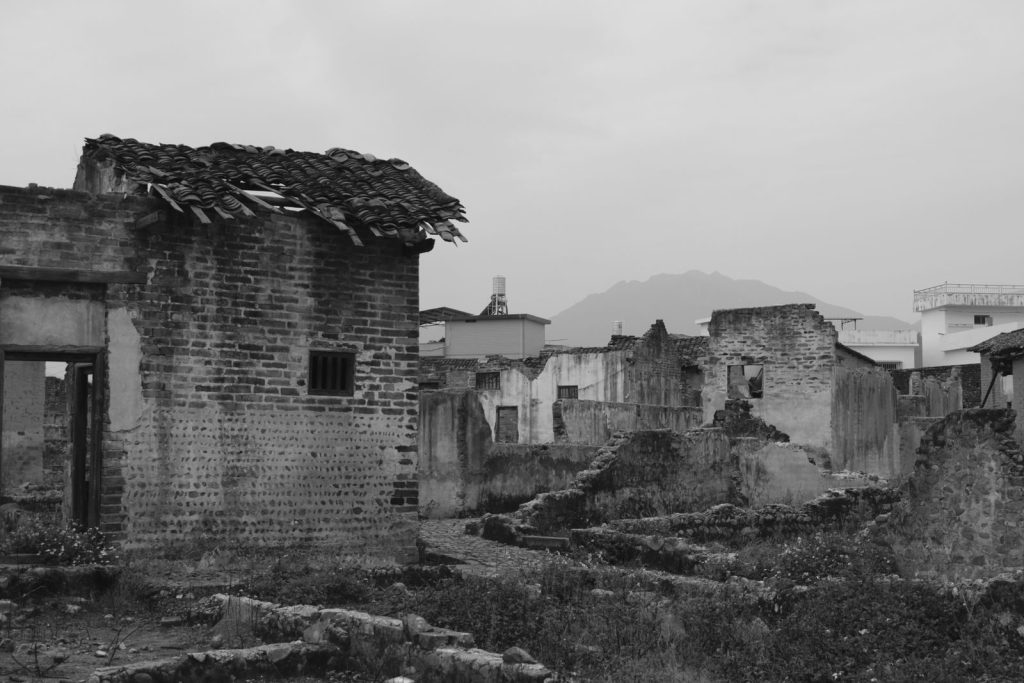 Monochrome photo showing abandoned buildings with visible decay and urban backdrop.
