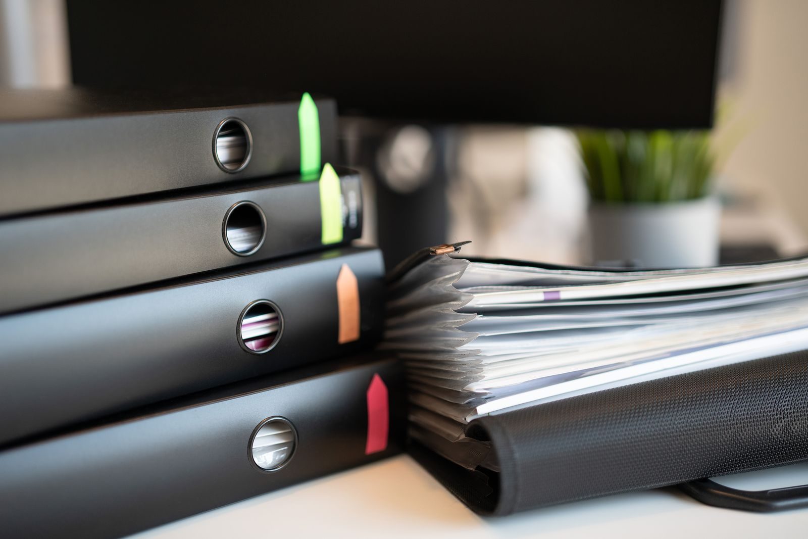 Stack of colorful ring binders and documents on a modern office desk setting.