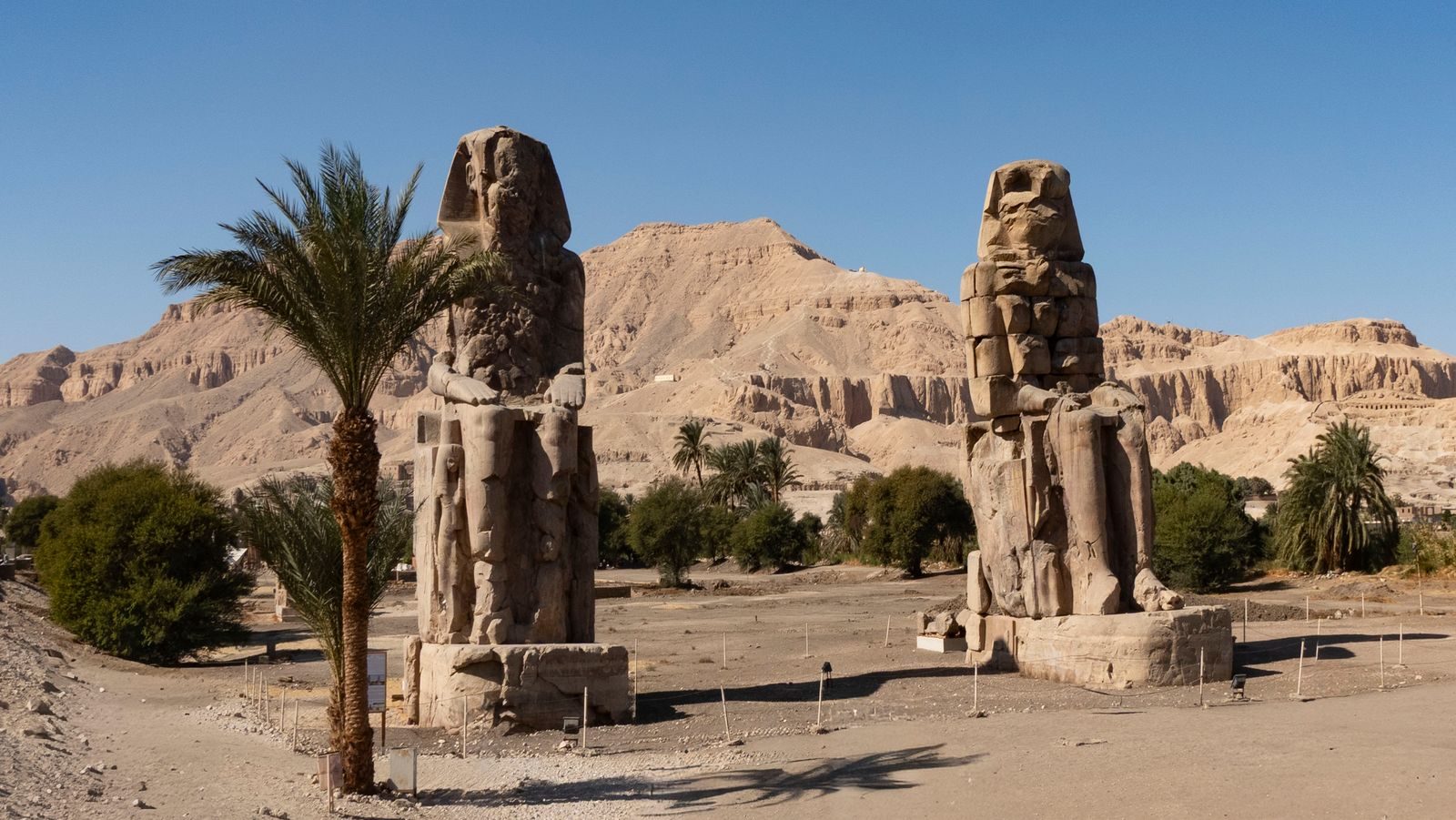 Explore the ancient Colossi of Memnon statues against rugged desert mountains in Luxor, Egypt.