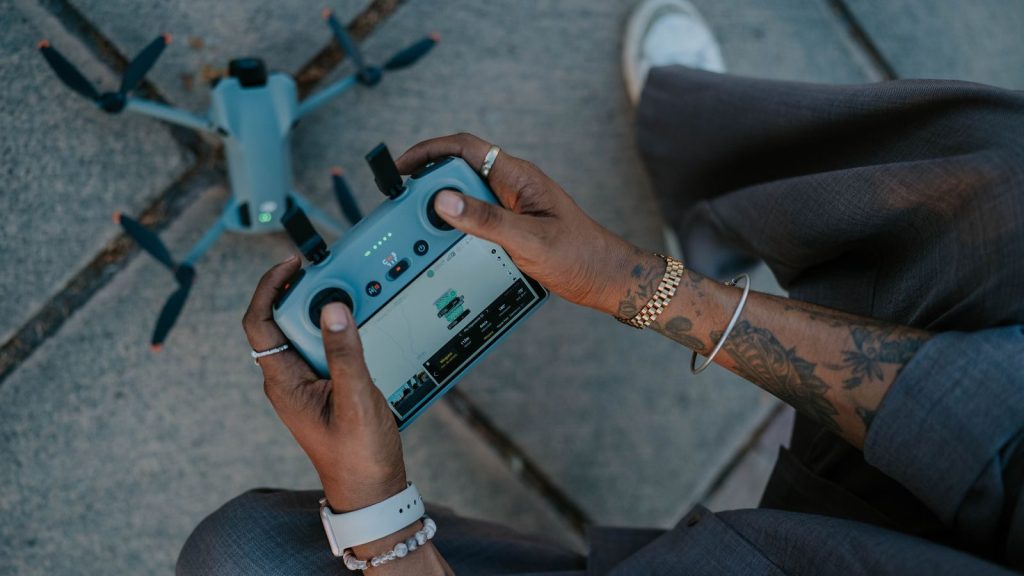 Tattooed hands operating a drone controller, emphasizing outdoor drone technology.