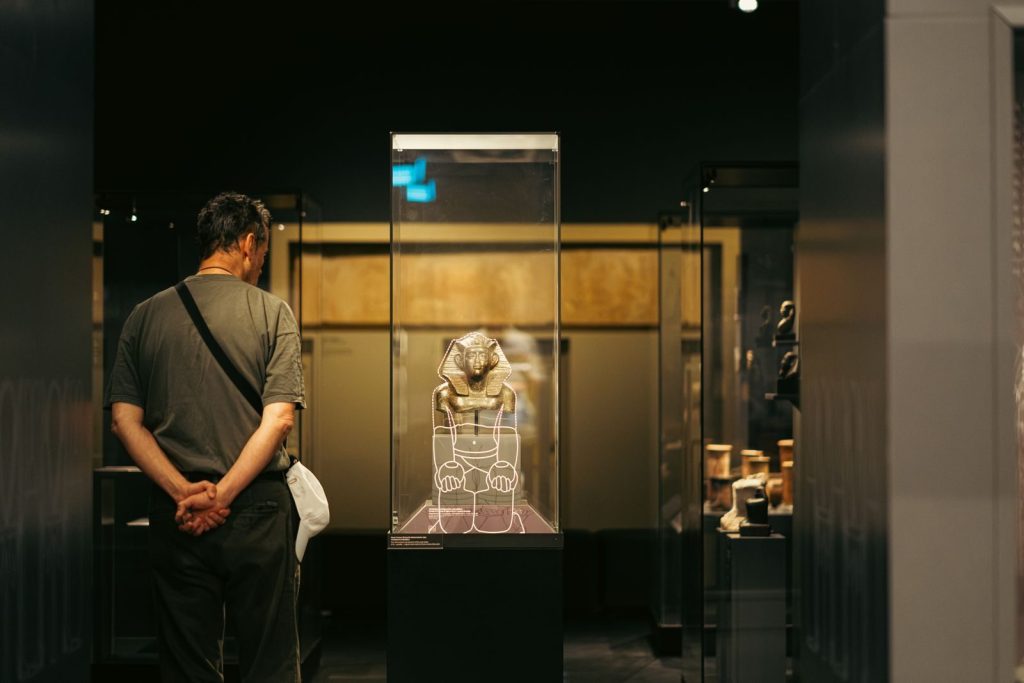 Visitor observing an ancient Egyptian artifact display in a Budapest museum exhibit.