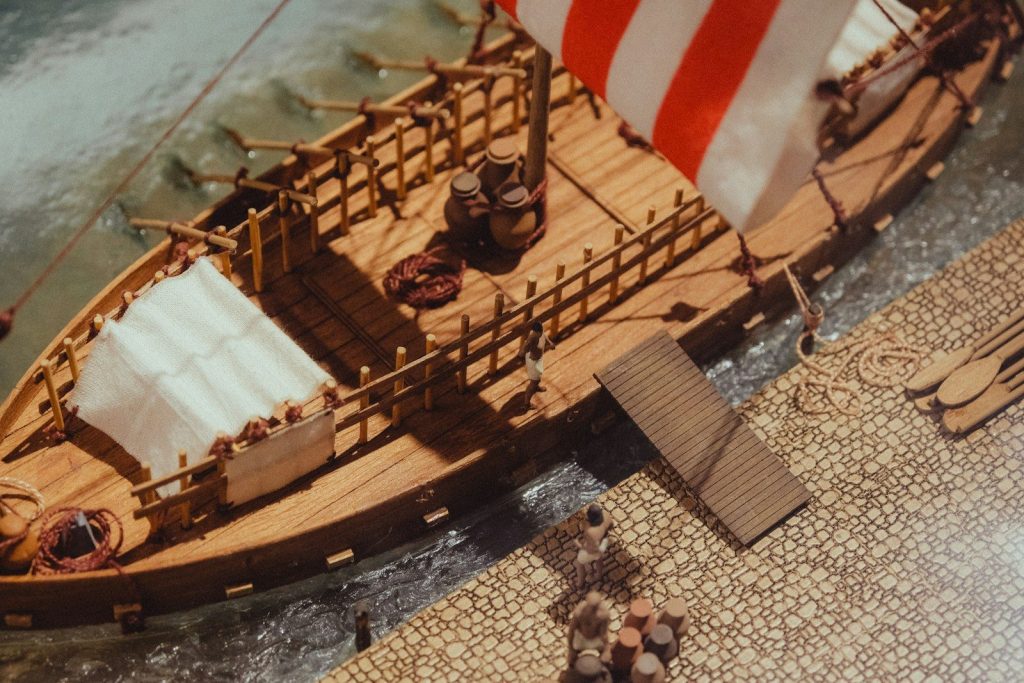 Wooden ship with red and white sails docked at shore.
