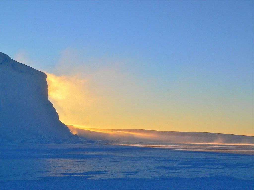 A breathtaking sunrise over Antarctic icebergs with a clear sky and serene atmosphere.