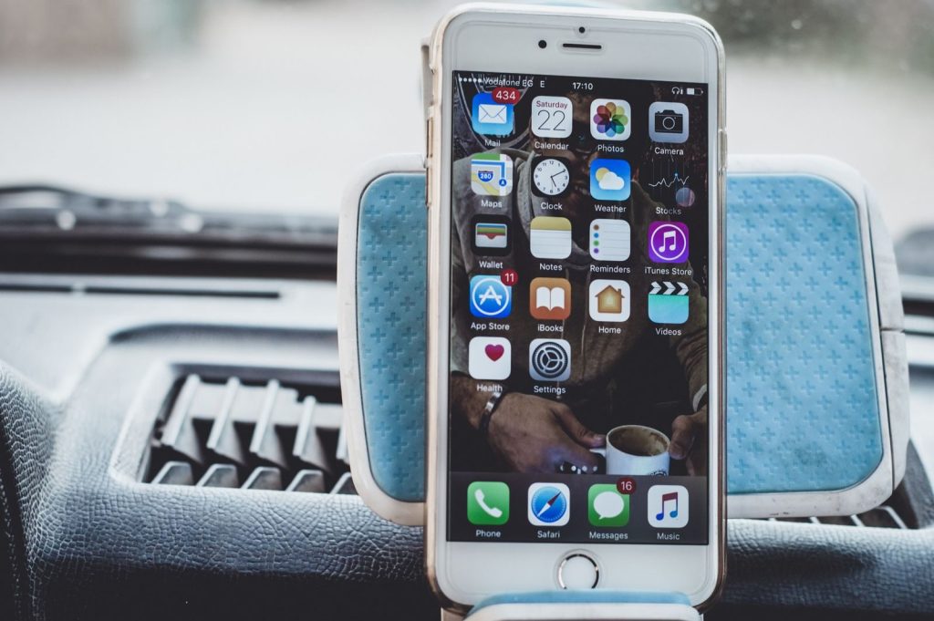 Close-up of a smartphone mounted on a car dashboard showing home screen with apps.