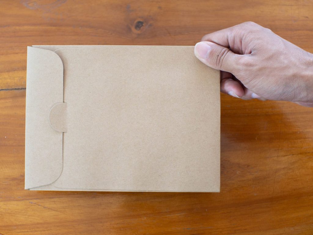 A close-up of a hand holding a brown envelope on a wooden table background.