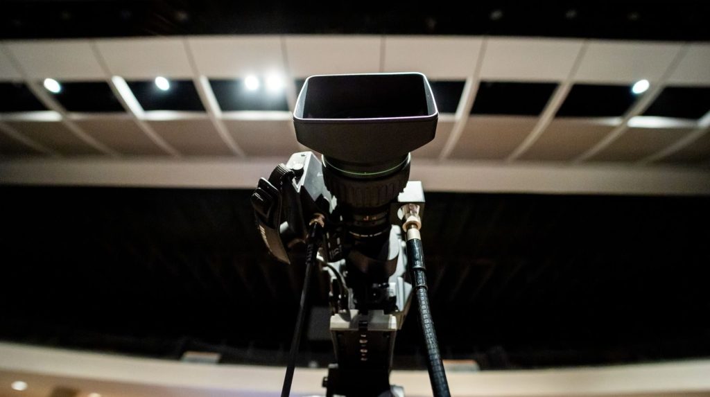 Low angle of professional video camera with lens on tripod placed under ceiling with lights in studio