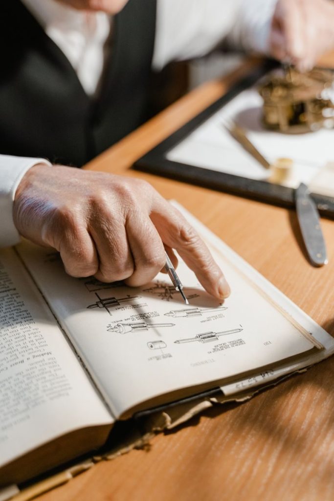Senior man pointing at a technical illustration in a book during study or research.