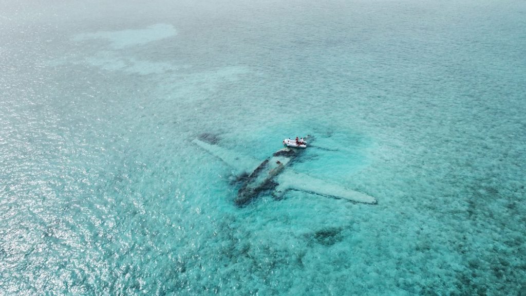 Drone shot of a sunken airplane beneath turquoise water, ideal for travel and adventure themes.