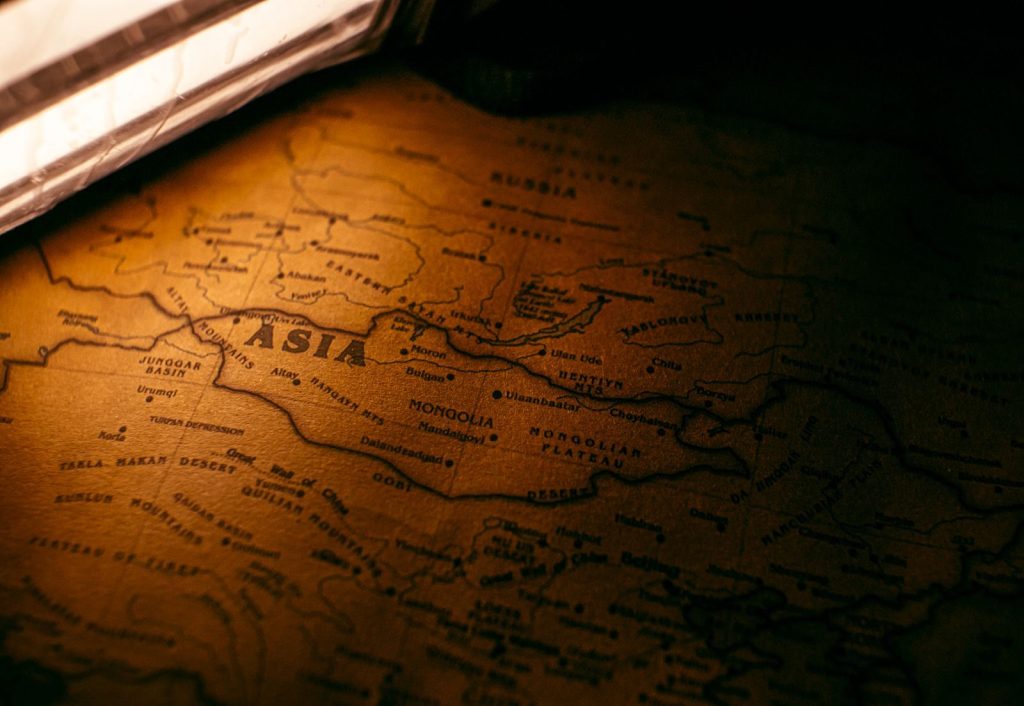 A close-up of a vintage map highlighting Asia, bathed in warm atmospheric lighting.