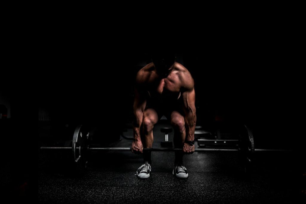 shirtless man lifting barbell in gym
