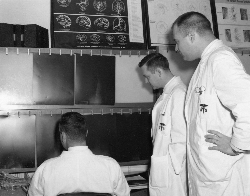 Three men in lab coats examine medical scans
