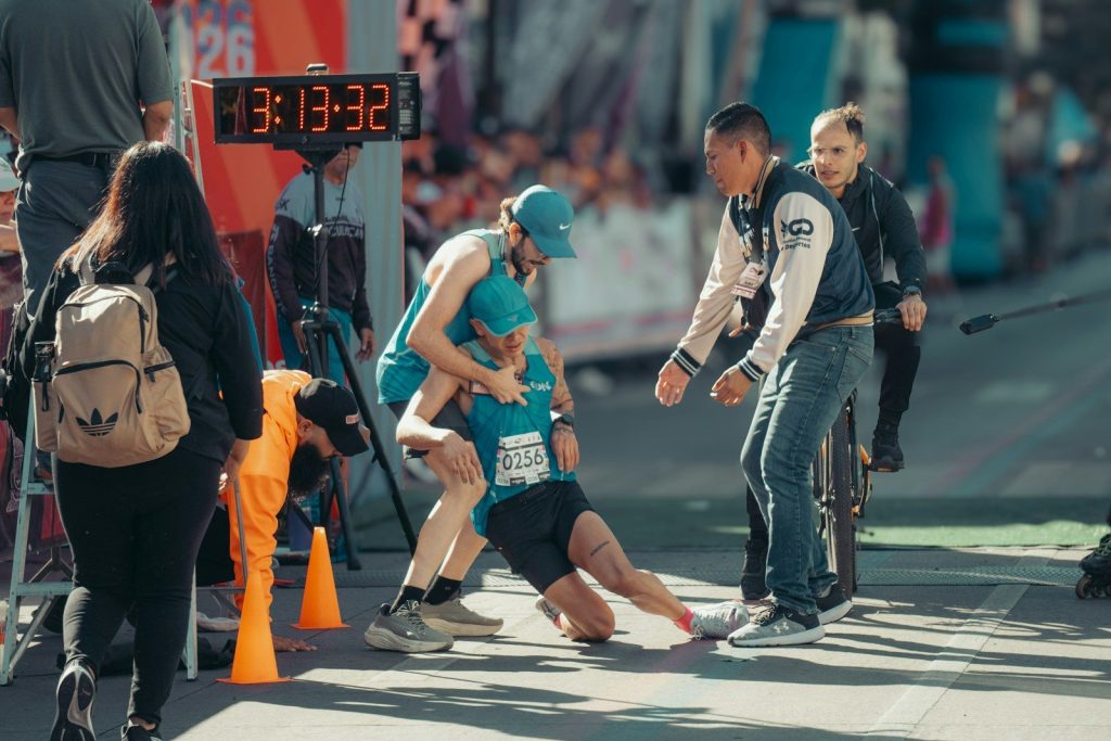 Runner collapses at finish line, helped by others.