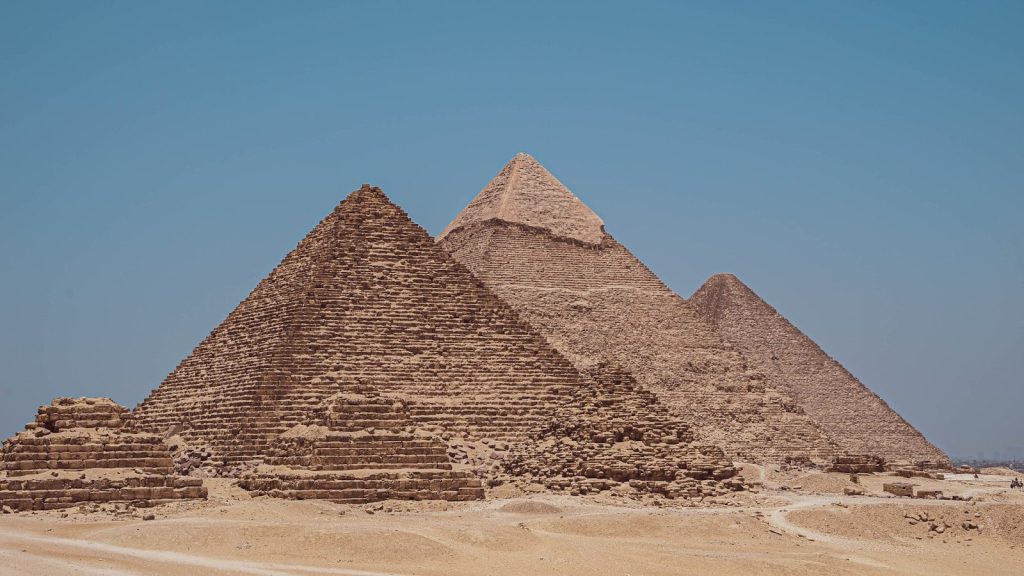 three pyramids in the desert with a blue sky in the background
