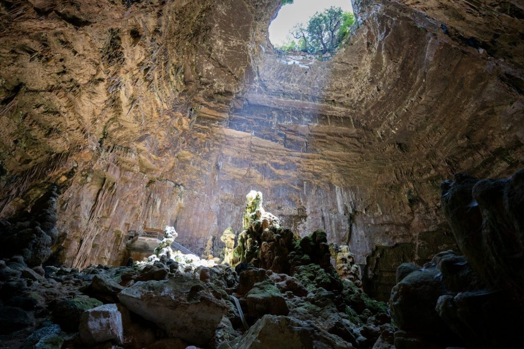 Sunlight streams into a vast cave with rock formations.