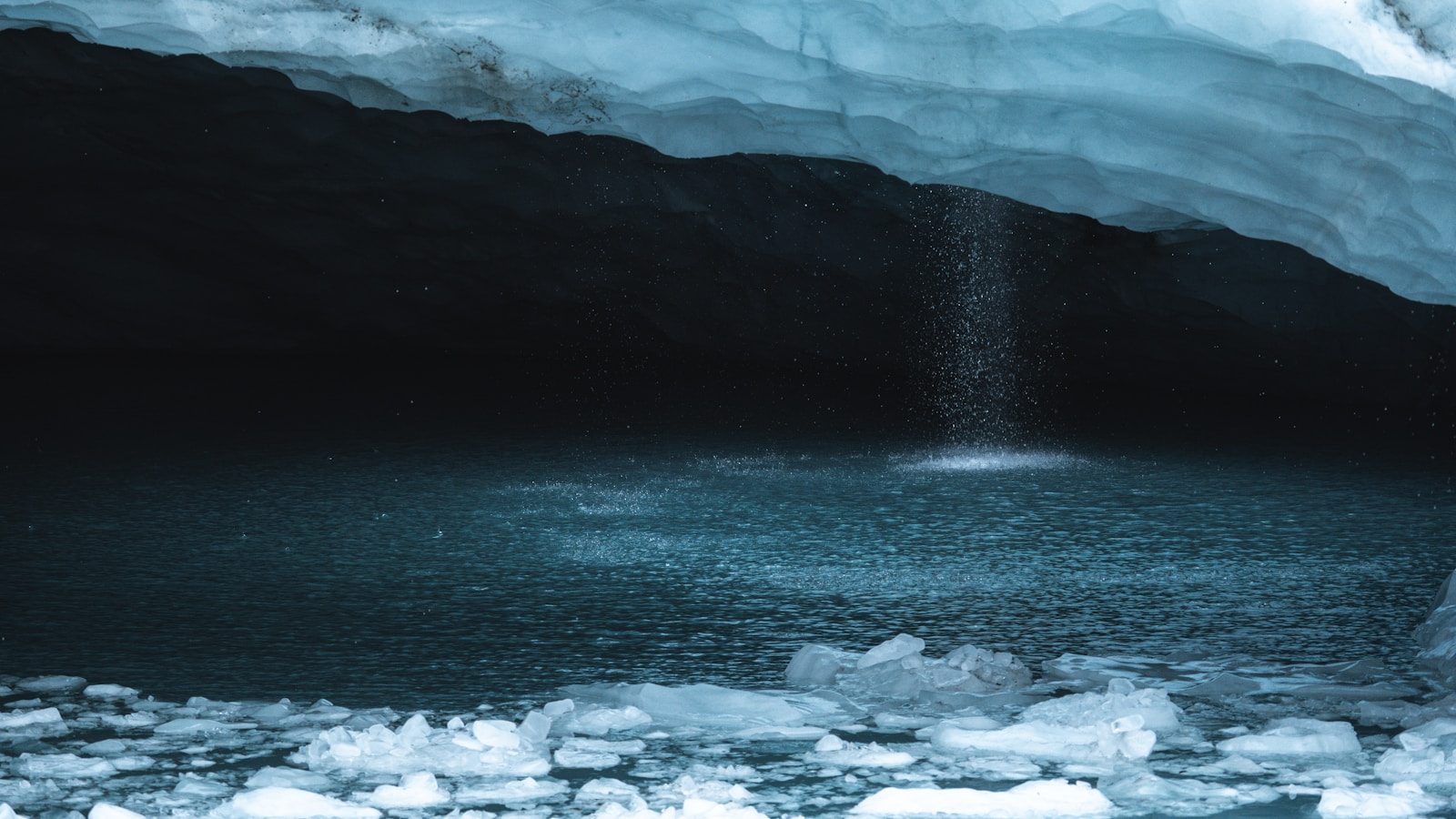 Water falling into a dark pool inside an ice cave.