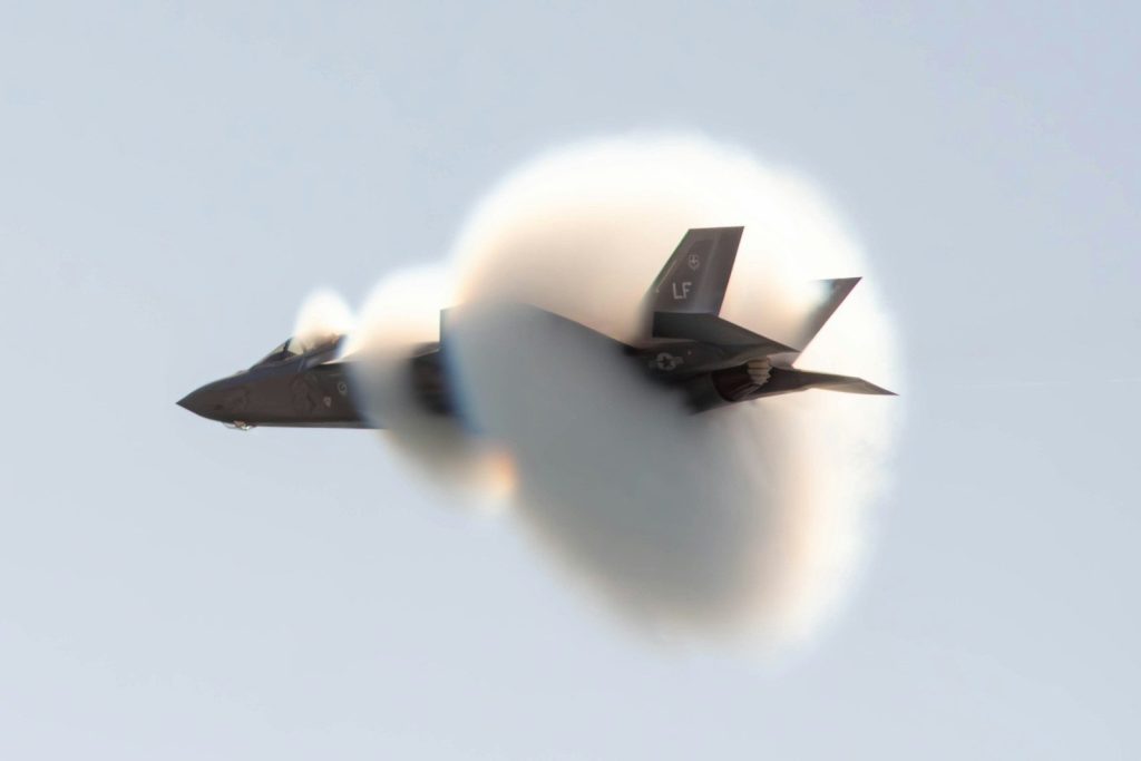 An f-35 fighter jet creating a vapor cone in flight.