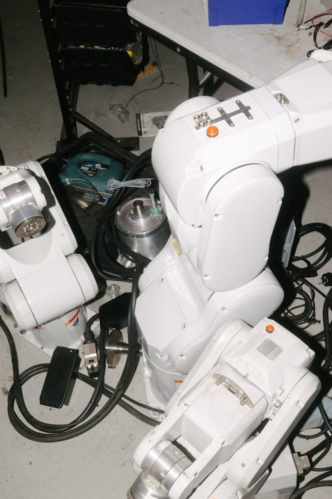 White robotic arms and tangled wires on a workshop floor.